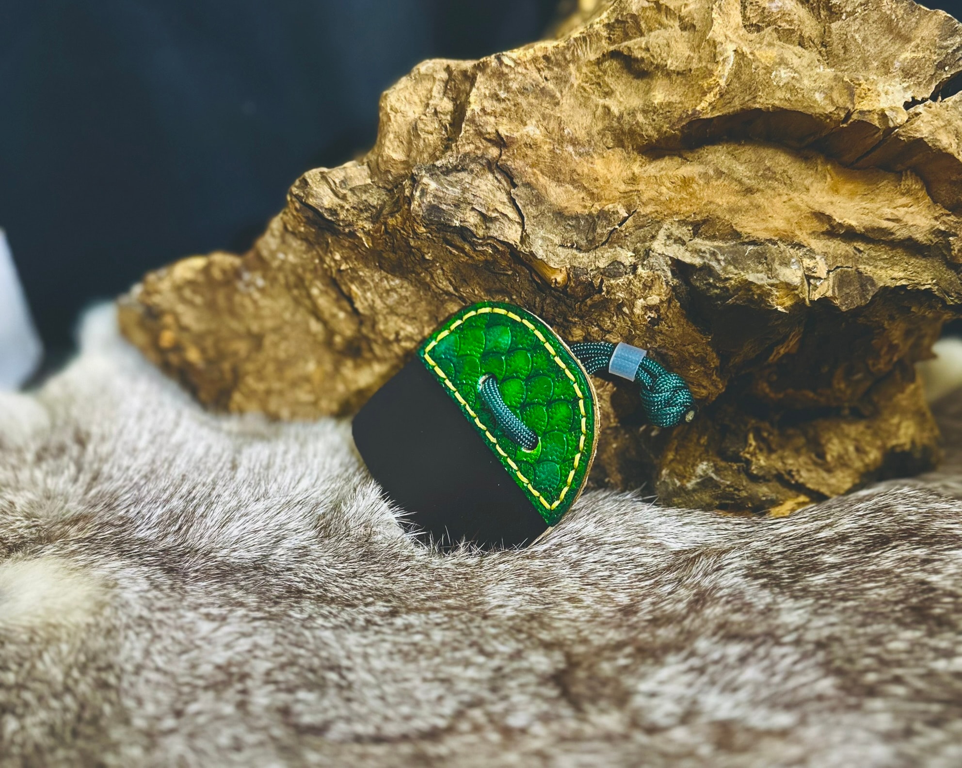 Dragon scale archery tab in vivid green with yellow stitching and teal paracord