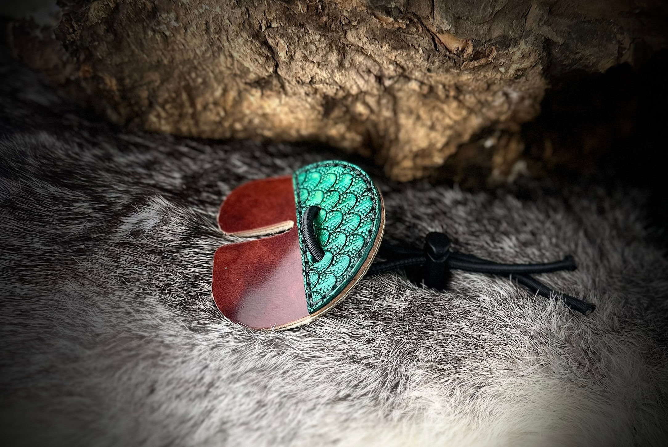 Teal dragon scale archery tab with cordovan leather and black paracord on grey fur