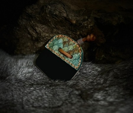 Dragon scale archery tab in teal with tan paracord, photographed on dark fur
